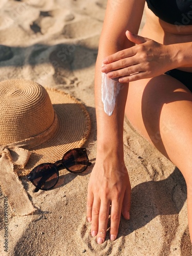Woman applying sunscreen lotion on her arm at the beach