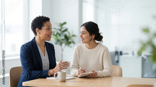 Two diverse businesswomen having a meeting in a modern office. Professional Black mentor talking to a Hispanic colleague. Mentorship and collaboration in the workplace