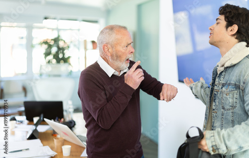 Fotografija Elderly man sternly scolds young male colleague for being late for work in offic