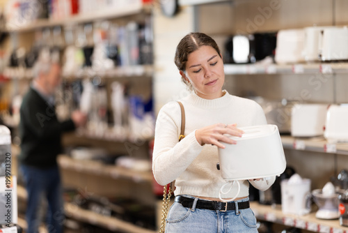Foto Positive young woman choosing toaster in hypermarket and smiling