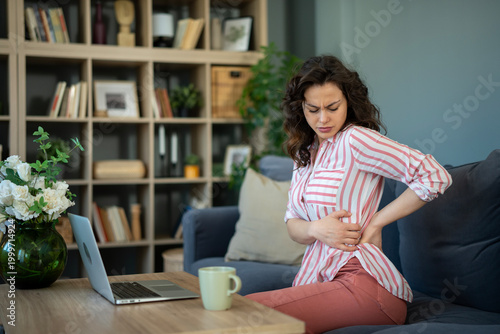 Foto Woman experiencing lower back and body pain sitting on sofa