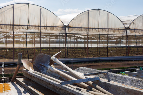 Metal shovels lying on wooden planks near large greenhouse