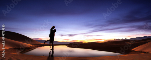 Romantic couple embracing at sunset in a desert with sand dunes and a reflective lake