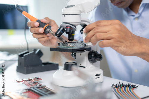 Electronics technician repairing circuit board using soldering iron and microscope
