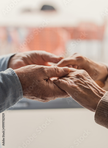 Картината върху платно Elderly couple hold hands in a tender gesture of support and compassion, conveying love, trust and gentle caregiving between partners in a quiet indoor setting