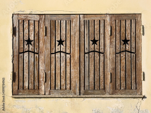 Weathered Brown Wooden Window Shutters with Star Cutouts on Pale Yellow Wall