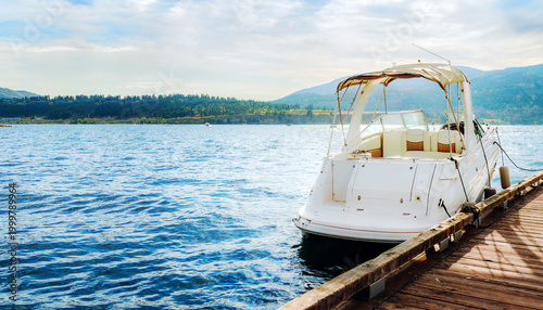 White motorboat moored at wooden pier on a beautiful lake with mountain background on a sunny day