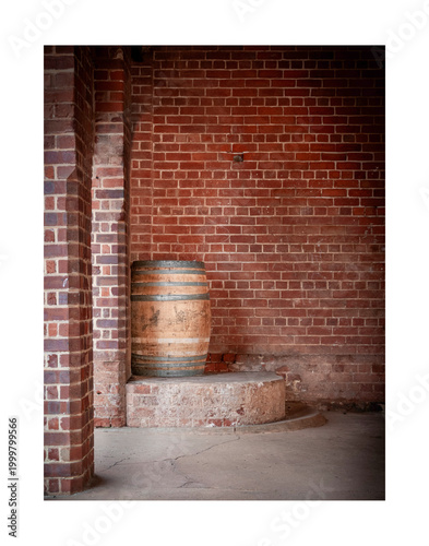 A solitary wooden barrel rests on a circular platform against a red brick wall. The shadows and textures create a rustic ambiance.