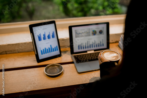 Professional woman working on laptop in café, enjoying hot drink break, smiling thoughtfully, balancing productivity, comfort, and modern lifestyle.
