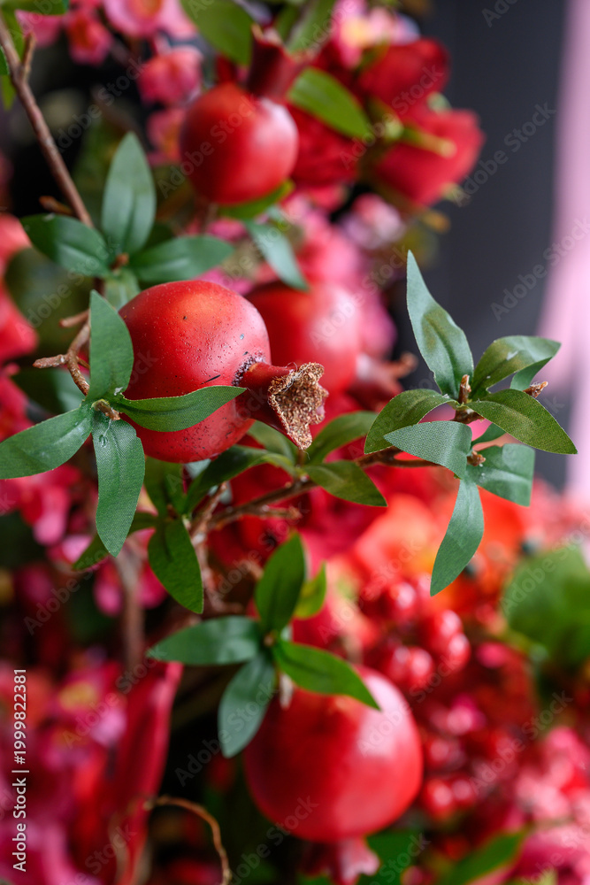 Obraz premium Pomegranates and flowers arranged together in a vibrant display indoors. Pomegranates and green leaves are part of a colorful floral arrangement in a bright setting.