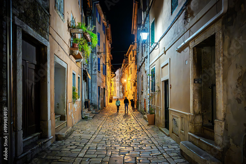 Photos A couple walks down a narrow cobblestone alley at night in the medieval old town center of the coastal city of Rovinj, Croatia