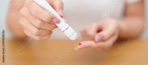 Photos Hand using lancet pen on finger with Blood drop glucose testing or Diabetes checking by digital blood glucose meter