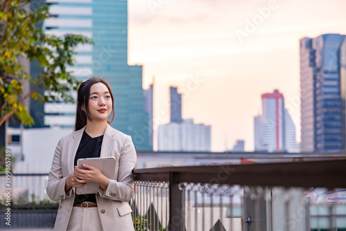 Luxury young Asian business woman entrepreneur using digital tablet while walking in the green building modern office downtown on background for communication and urban lifestyle