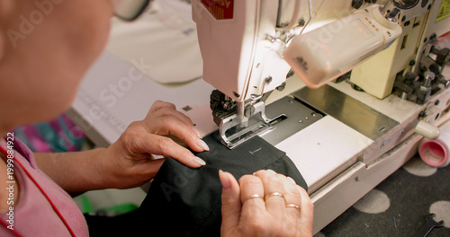 Clothing making. Sewing process. Tailor working on stitching professional machine. Woman creating buttonhole on black fabric sleeve.