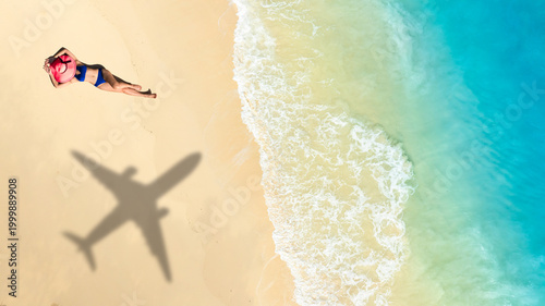 Tableau sur toile Top view of a woman in bikini blue sunbathing on white sand beach with a large airplane shadow over her; concept of dream summer vacation, air travel, and tropical island holiday destination