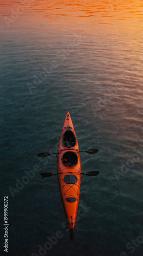 kayak in calm sea reflecting orange-pink sunset sky