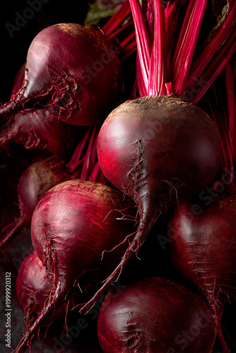 A cluster of freshly harvested beets showcases vibrant red and purple colors. The beets rest on a dark surface, with rich green leaves adding contrast.