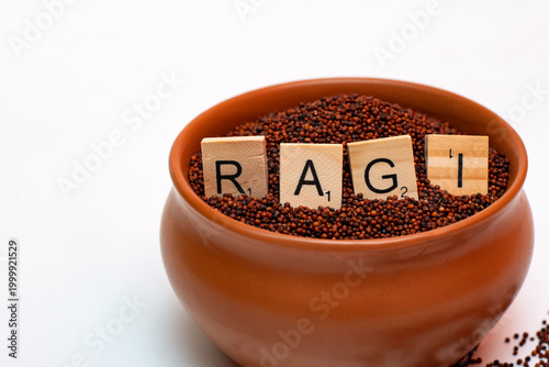 Clay pot filled with ragi millet grains and wooden RAGI letters on white background