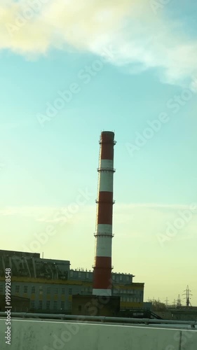 Tall red-white striped industrial chimney at power plant, urban skyline and blue sky backdrop