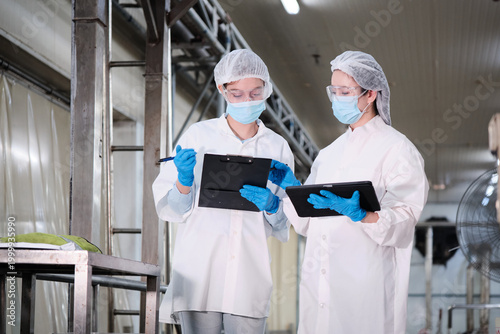 Two female industrial engineers coworkers inspect and examine quality control, production machines in food manufacturing factory, clean and protective uniforms for maintenance, and evaluate operation.
