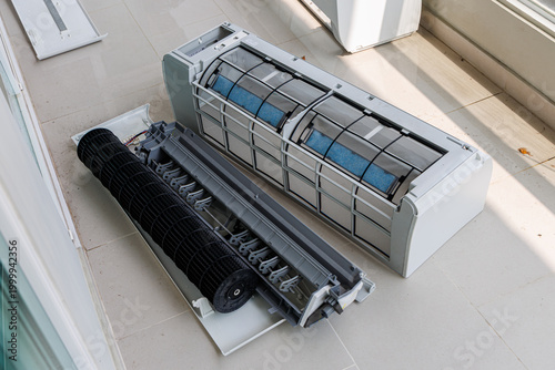Professional technician using a high-pressure water sprayer to deep clean the evaporator coils of a wall-mounted air conditioner unit.