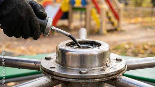 Person applying grease to merry-go-round at playground equipment  