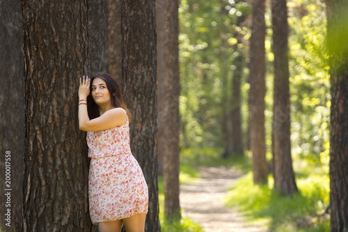 A young woman walking in the forest. A beautiful woman resting in a forest, leaning against a pine tree trunk.