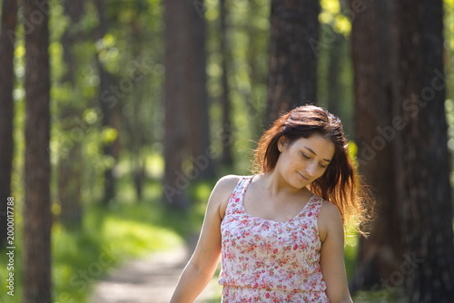 Portrait of a young woman in a park. A pretty woman stands on a path between pine trees, looking down, smiling mysteriously.