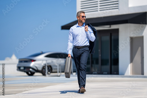 Corporate business. Rich businessman suit. Business success. Successful businessman walking with briefcase. Businessman hold briefcase. Confident businessman in suit after successful deal