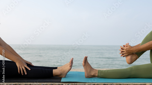 Fotografija Two people are sitting on mats by the ocean, each performing a stretching exercise