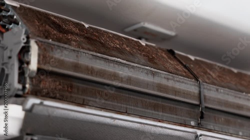 High-pressure water spray cleaning a dirty air conditioner filter to remove thick dust and improve indoor air quality.