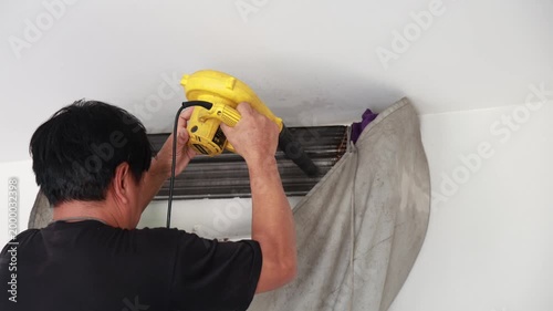 Professional technician using an electric air blower to dry the evaporator coils and internal components of a wall-mounted air conditioner after deep cleaning.