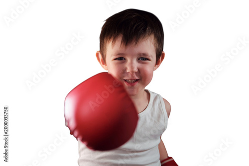 This determined child athlete trains hard, wearing red gloves and a white vest. With courage in his stance, the young boy practices his punches under studio lights. Kid aged three years (3 years old)
