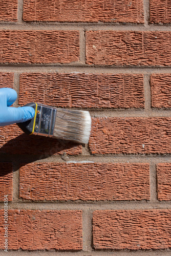 Person sealing an exterior brick wall with a clear waterproof sealant, using a paint brush. Do it yourself home improvement concept.
