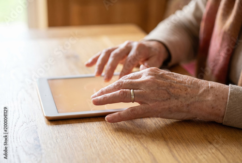 Elderly woman hands touching tablet screen on warm wooden table close up