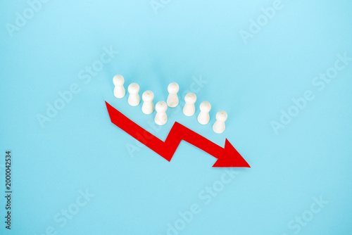 фотографія Line of wooden peg dolls stands behind red downward arrow on blue surface