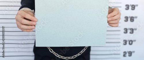 Foto Individual holding a blank piece of paper handcuffed in front of a height chart