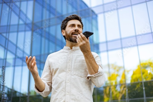 Obraz na płótnie A man with a beard speaks into his smartphone held to his ear while gesturing wi