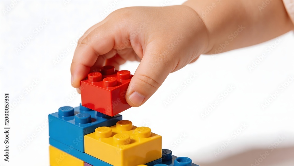 Fototapeta premium Childs hand placing red LEGO block