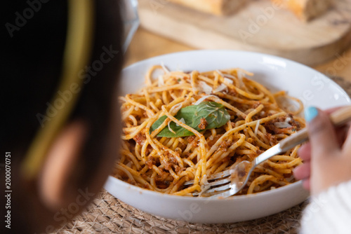 Child holding fork with turquoise nails, twirling spaghetti with basil in white bowl at table