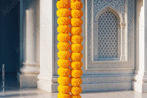 Bright yellow marigold flower garland hanging in sunlight against ornate stone architectural background with intricate patterns and columns. Ai generative
