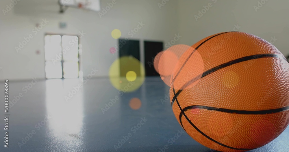 Fototapeta premium Resting orange basketball sitting on shiny blue court at gym, hoop visible, copy space