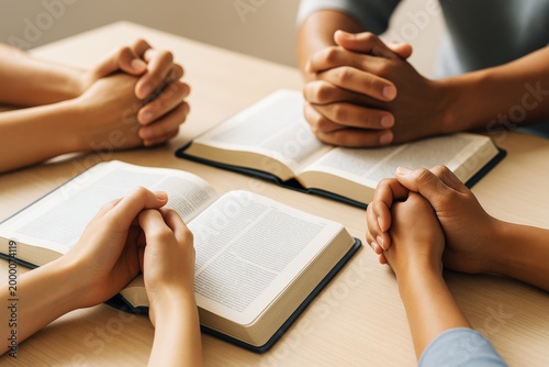 Group of diverse people praying together with open books on table under warm light, symbolizing unity, faith, and spiritual connection.