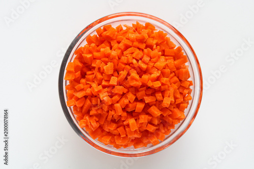 Top view of a clear glass bowl of diced orange carrots, isolated on a white background.