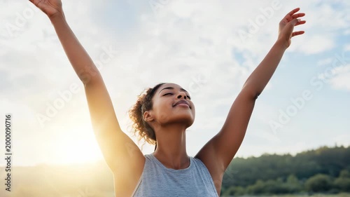 Young african female adult raising arms outdoors at sunrise in a sleeveless top, joyful expression and open landscape for morning fitness, stretching, and energetic wellness