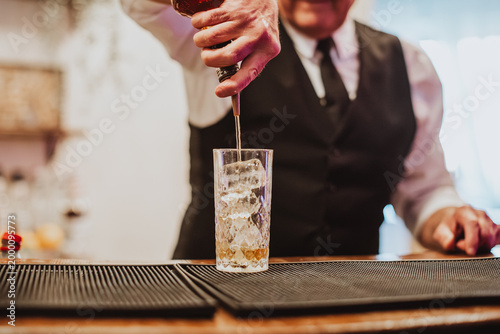 Bartender pours liquor into a tall glass filled with ice on a bar mat, creating a polished event drink service scene