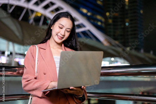 Asian young businesswoman using laptop computer outdoors in the city. 