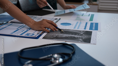Medical team in scrubs reviewing patient charts and lab reports on desk with laptop showing digital anatomy scan in hospital office.