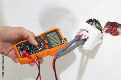 Schilderij op canvas Close-up of a professional technician's hands using a digital multimeter to check the voltage in a power socket during home electrical repair or maintenance