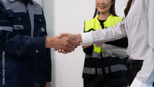Canvastavla Business handshake between client and engineer, with safety supervisor in reflective vest holding clipboard in background, representing partnership and workplace compliance